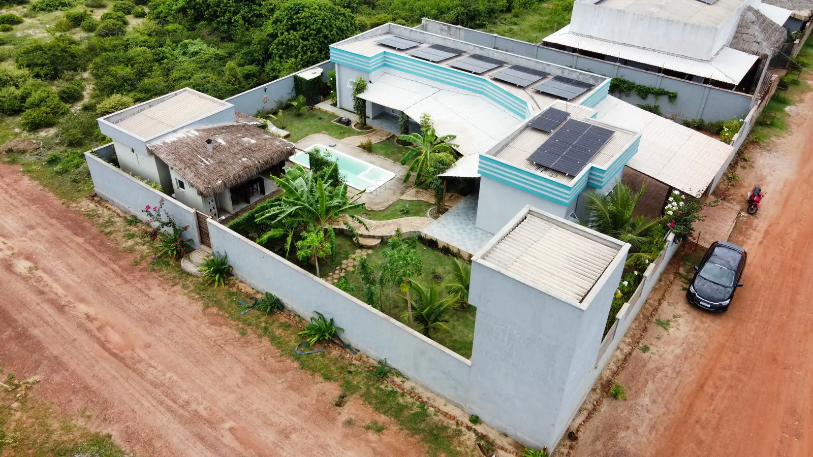 Aerial view of the walled villa with pool, solar panels and garden beside a red-earth street