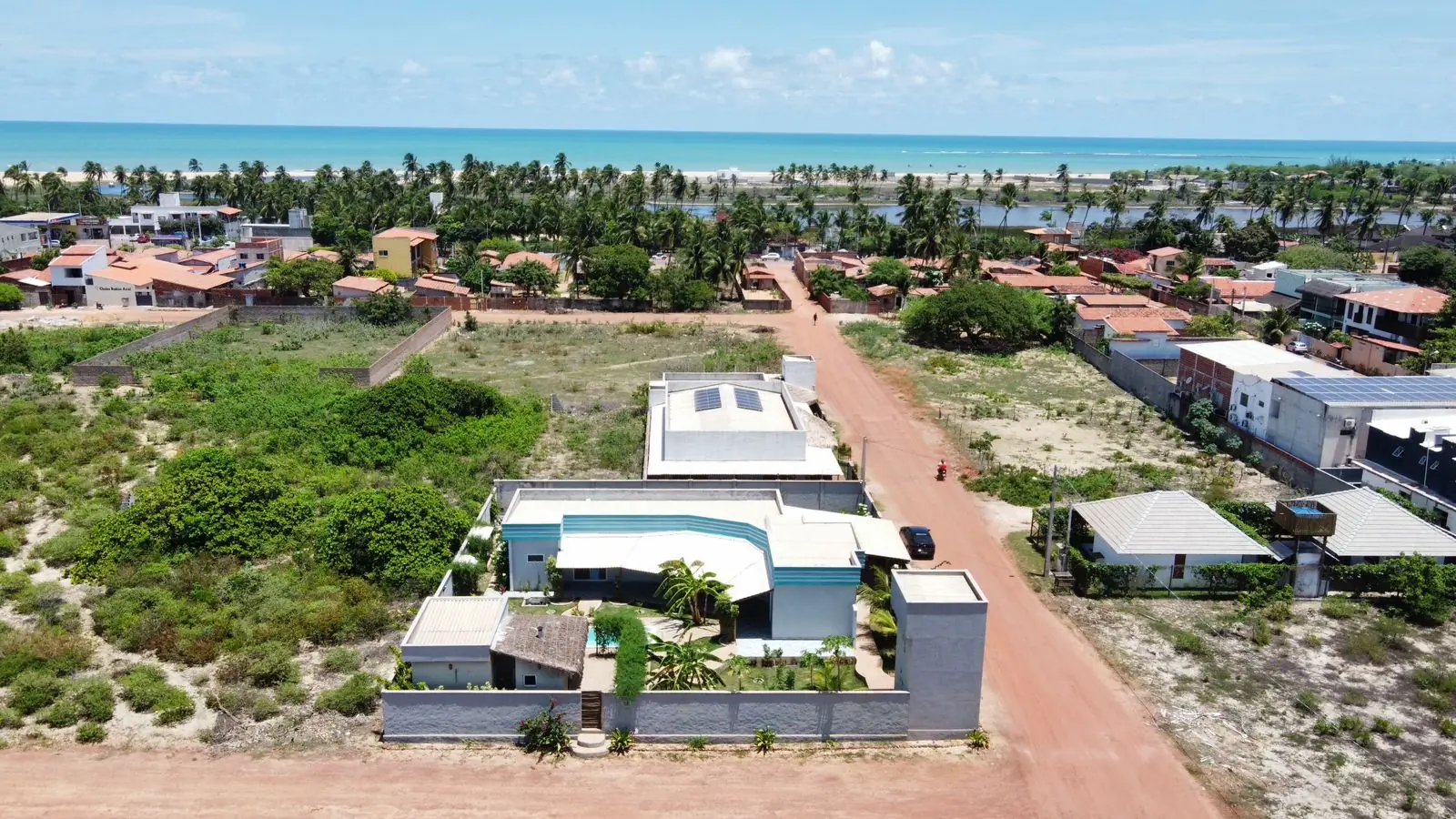 Aerial view over the village rooftops and scrubland to the coconut palms and the sea beyond