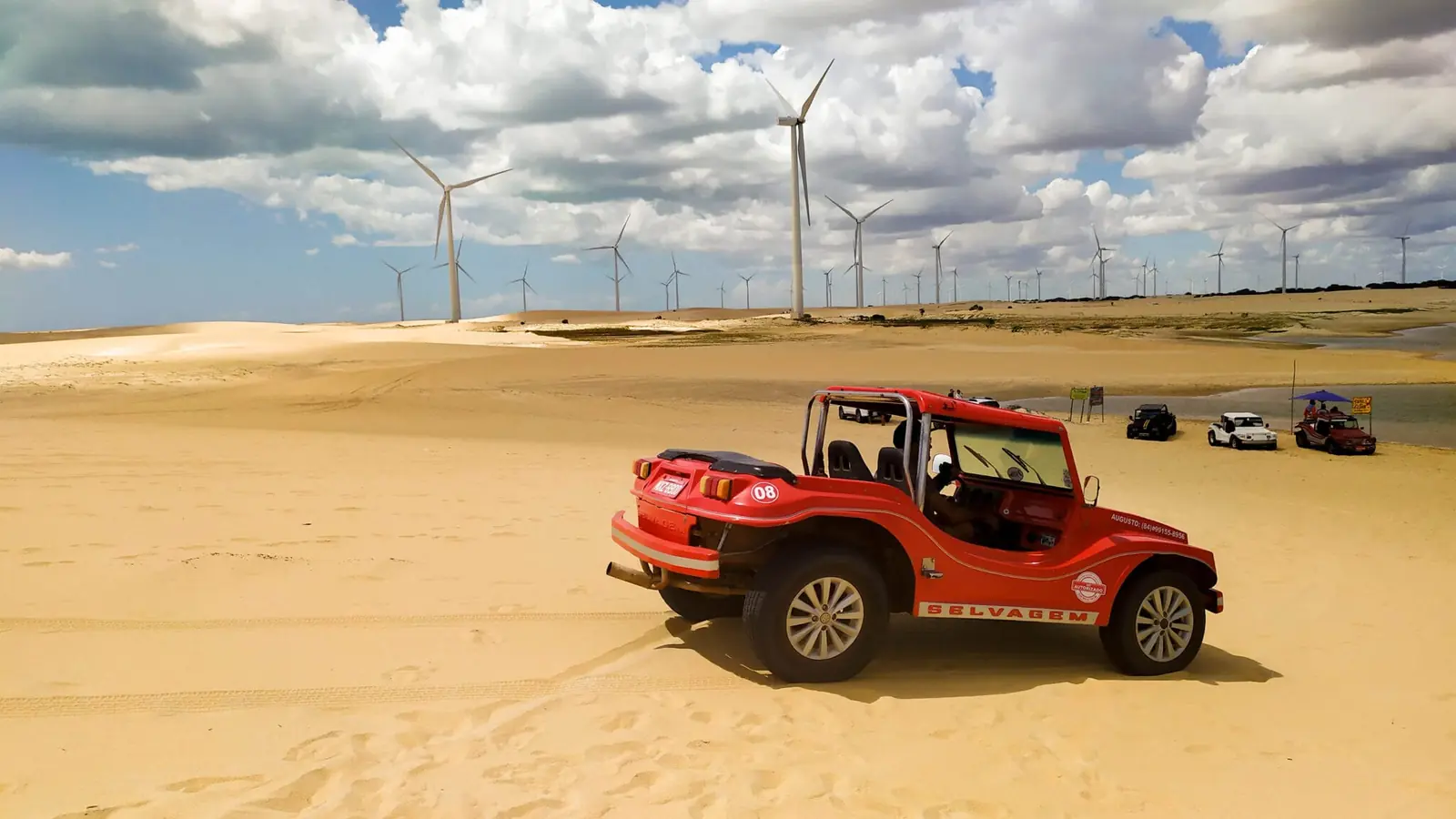 Red beach buggy on sand dunes with wind turbines on the horizon
