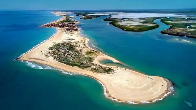 Aerial view of a sandy spit with a lighthouse between the open sea and a lagoon