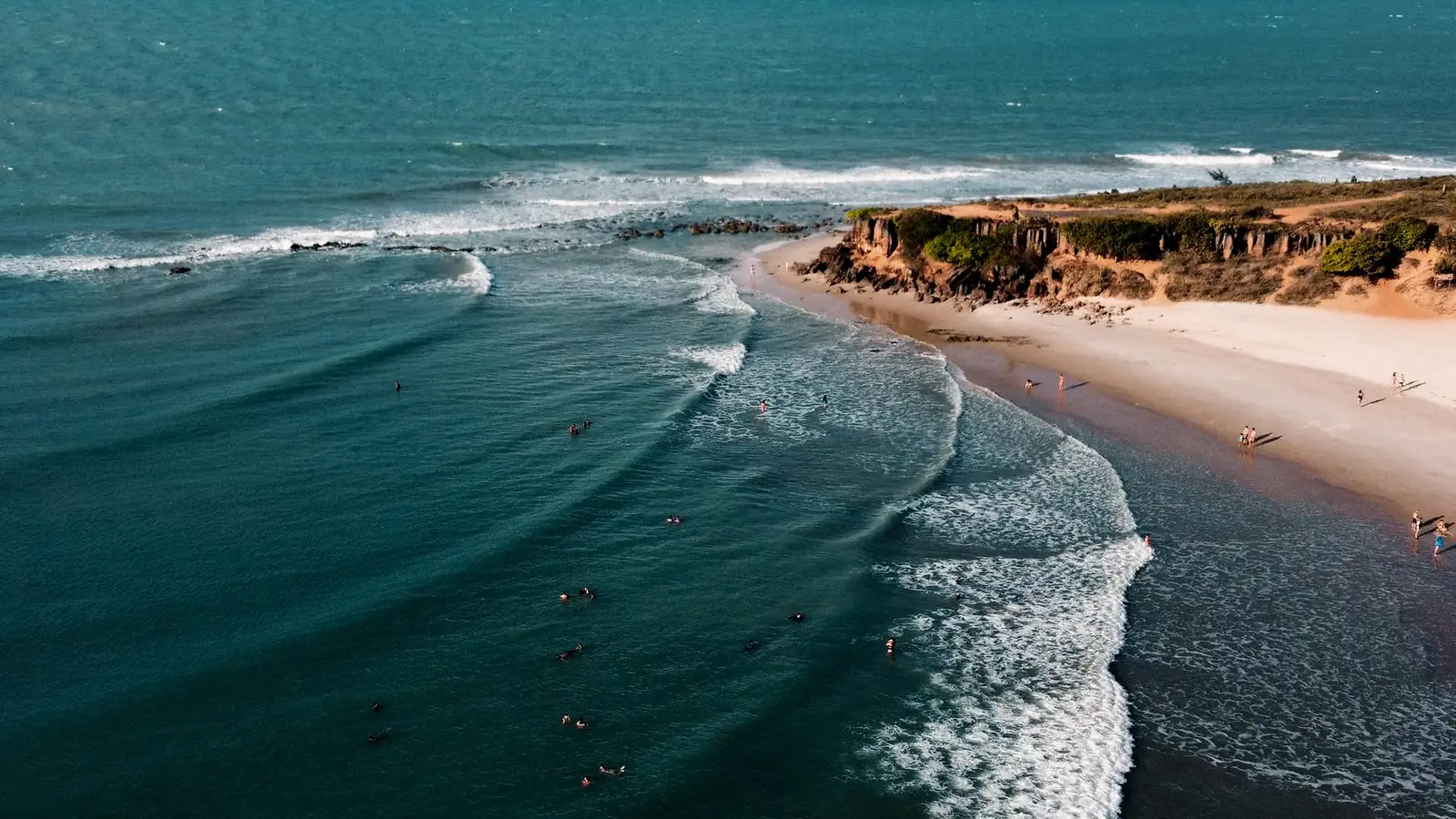 Aerial view of waves breaking at a river mouth with surfers and a sandy point