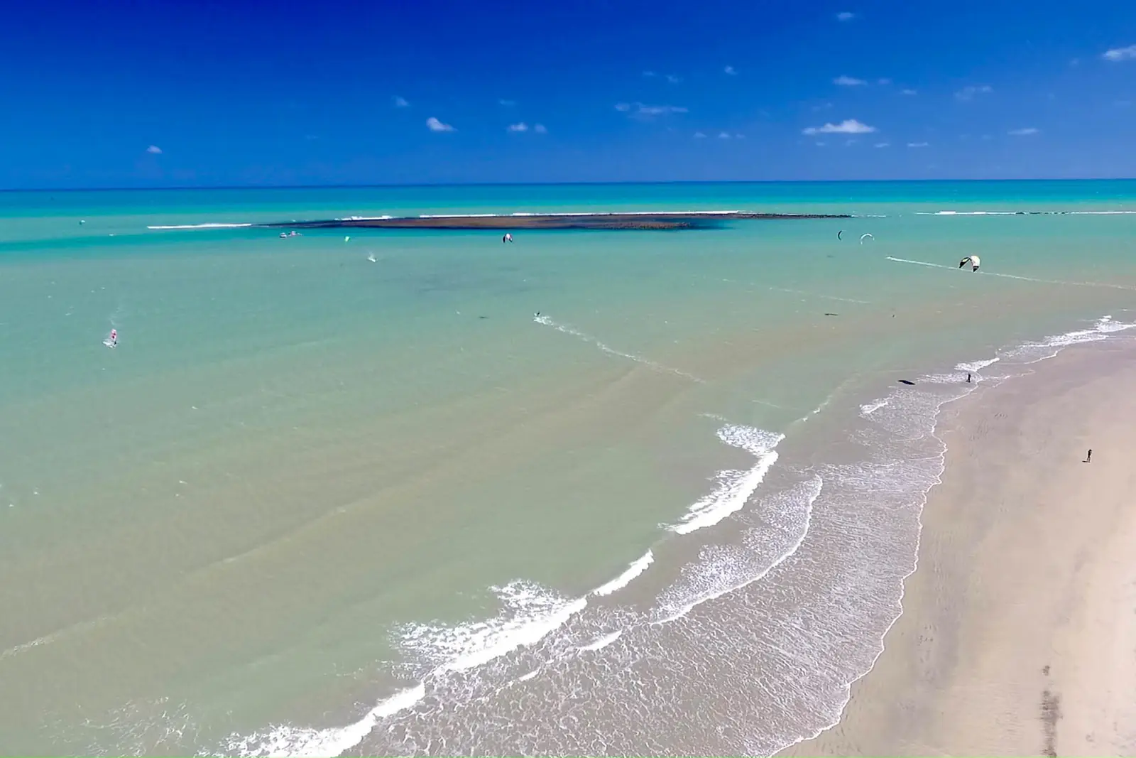 Turquoise sea with a sandbar offshore and a wide empty sandy beach