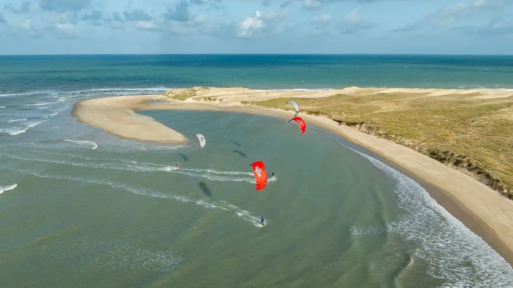 Aerial view of kitesurfers on a river mouth beside a sandbar and the sea
