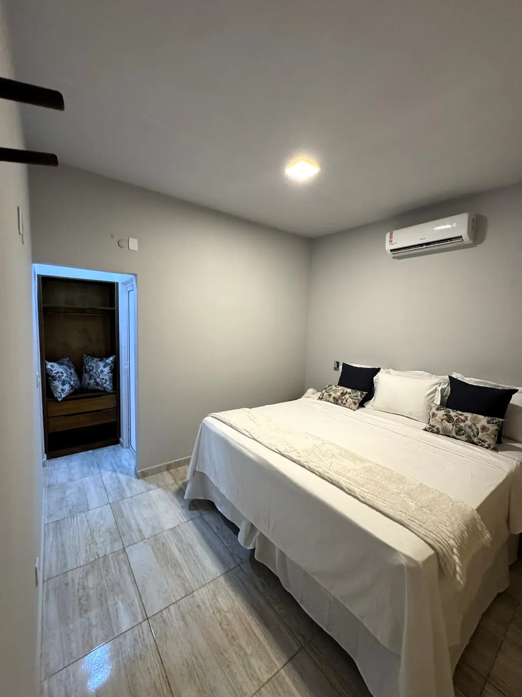 Bedroom with a king bed in white linen, wall air-conditioning unit and a doorway to the wardrobe