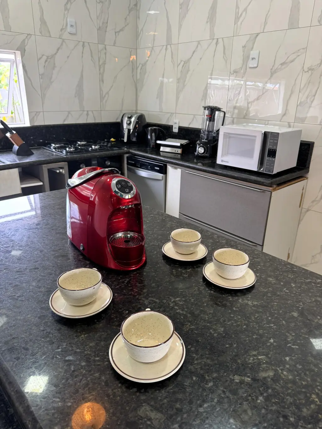 Kitchen counter with a red capsule coffee machine, cups and saucers, microwave and kettle behind