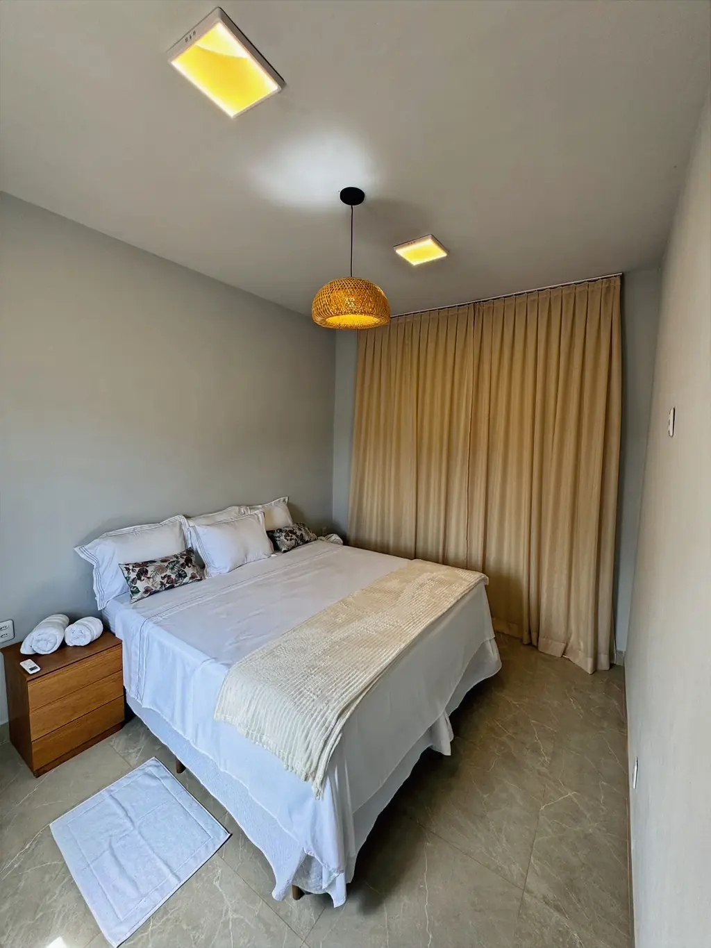 Bedroom with a king bed in white linen, a wicker pendant lamp and floor-length beige curtains