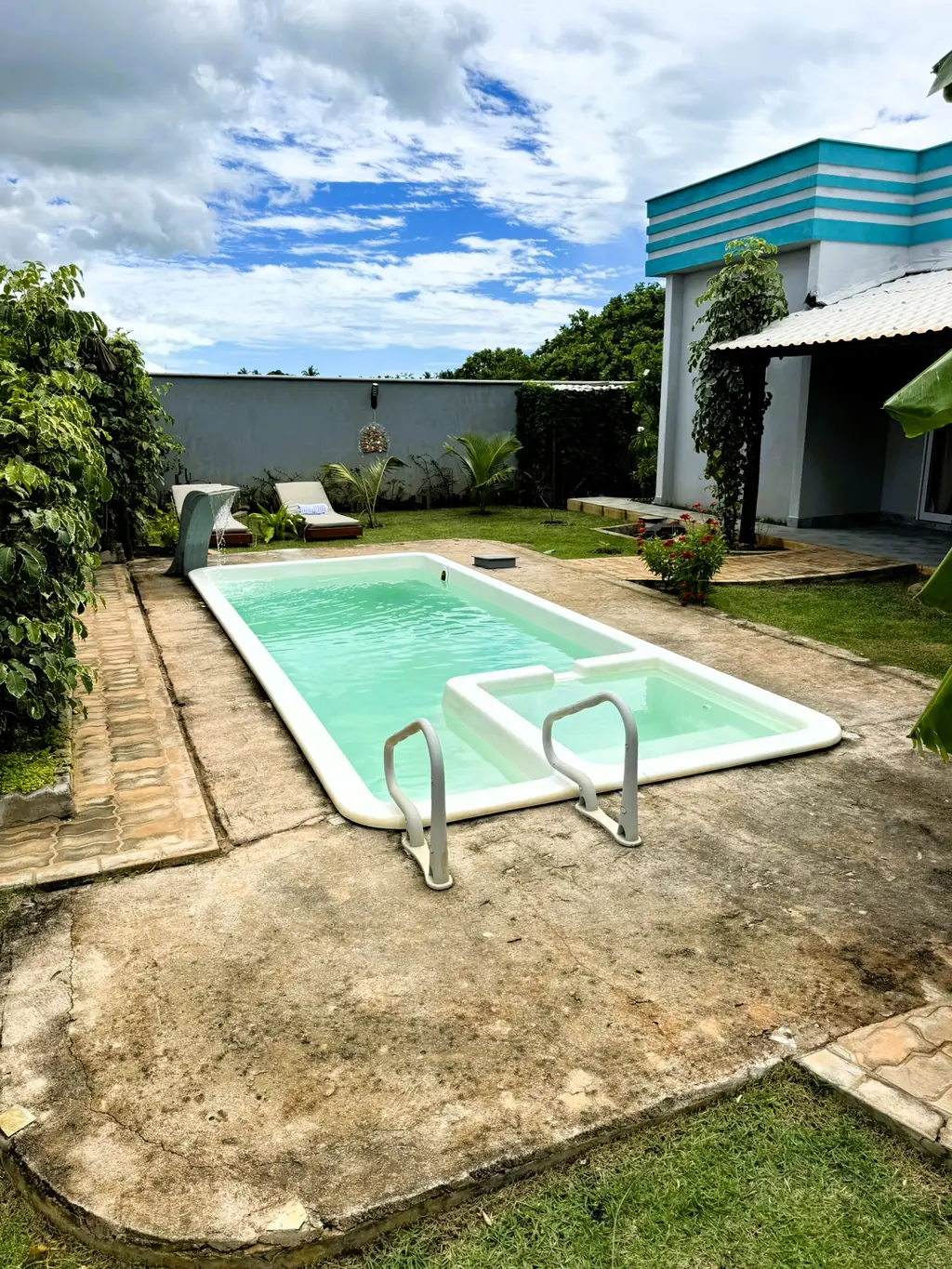 Pool with a stone surround and steel ladder beside the lawn, house with striped parapet behind