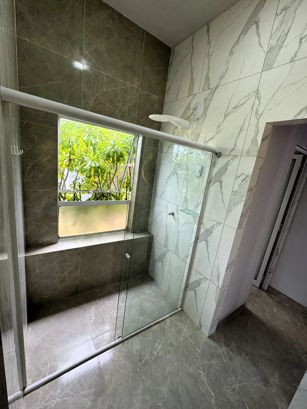 Walk-in shower with glass screen, dark marble-look tiles and a window onto greenery