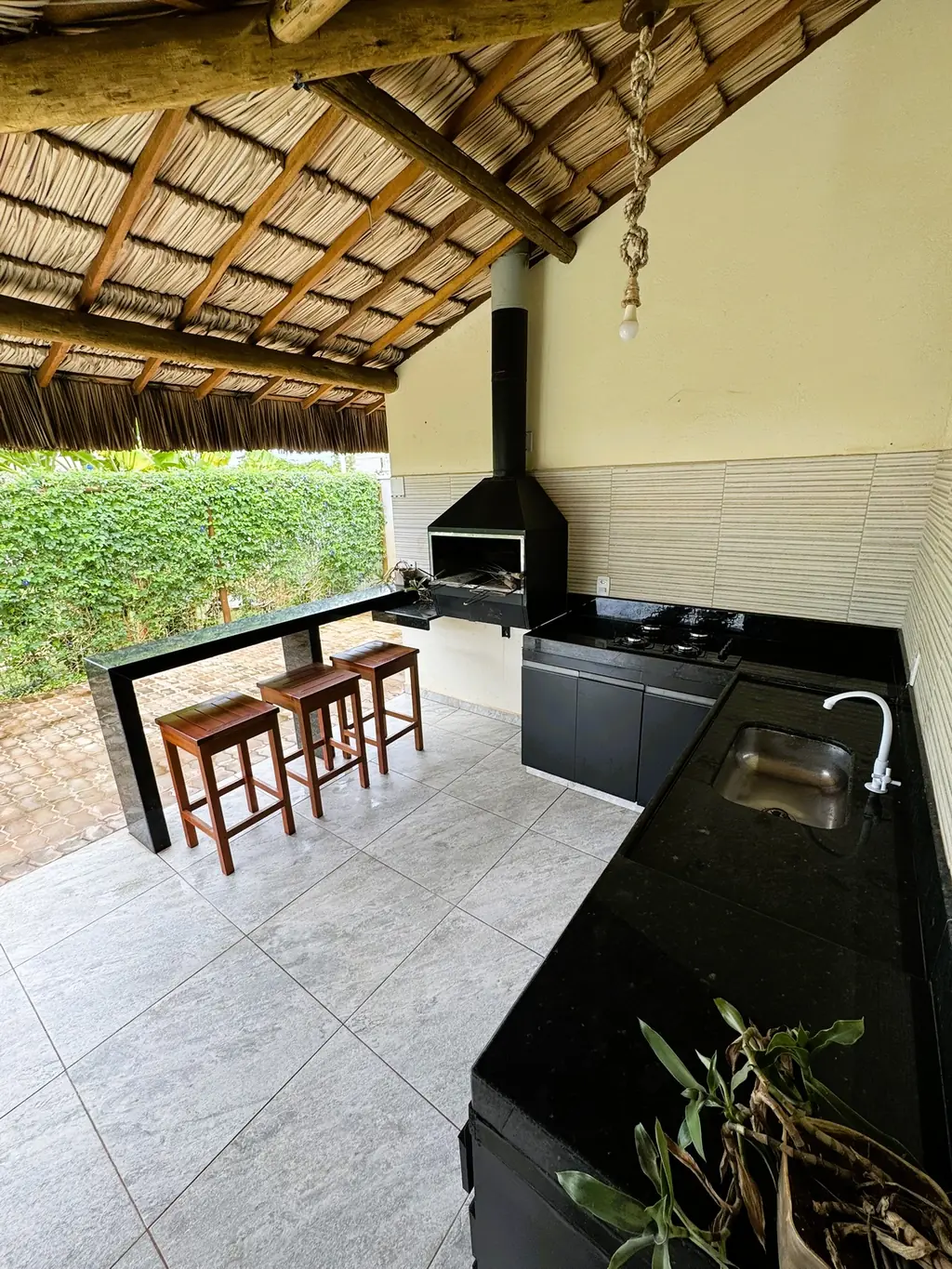Covered BBQ bar area with thatched roof, black stone counter with sink and two wooden stools