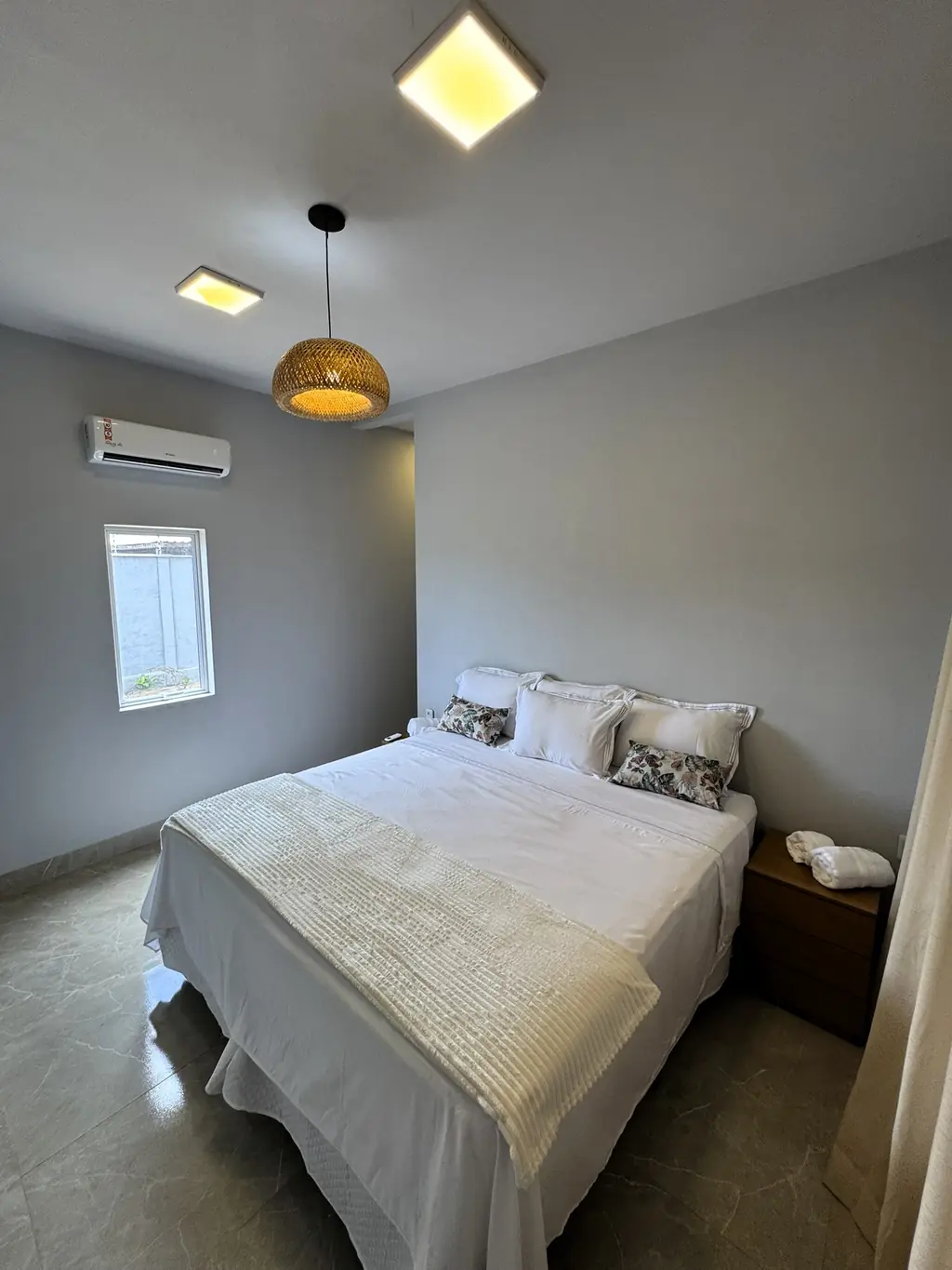 Bedroom with a king bed in white linen, air-conditioning unit, pendant lamp and a window